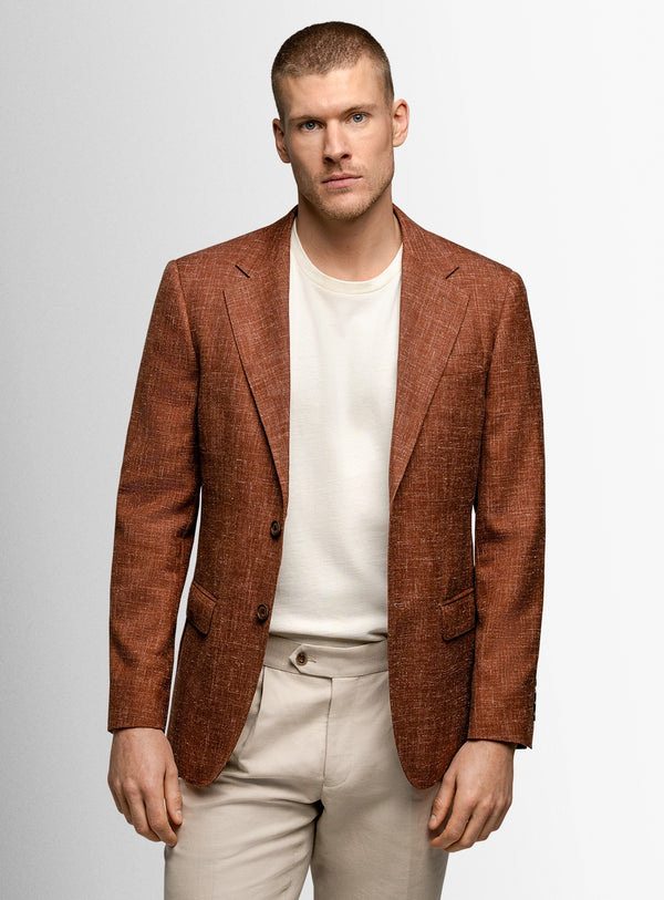 Man wearing a brown blazer over a white shirt and beige pants on a light gray background