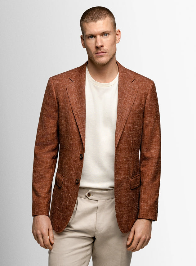 Man wearing a brown blazer over a white shirt and beige pants on a light gray background