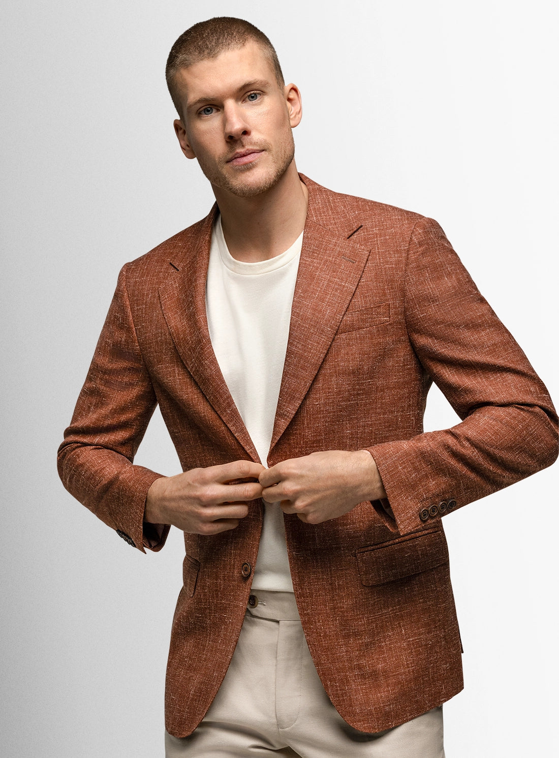 Man wearing a brown blazer over a white shirt on a light gray background