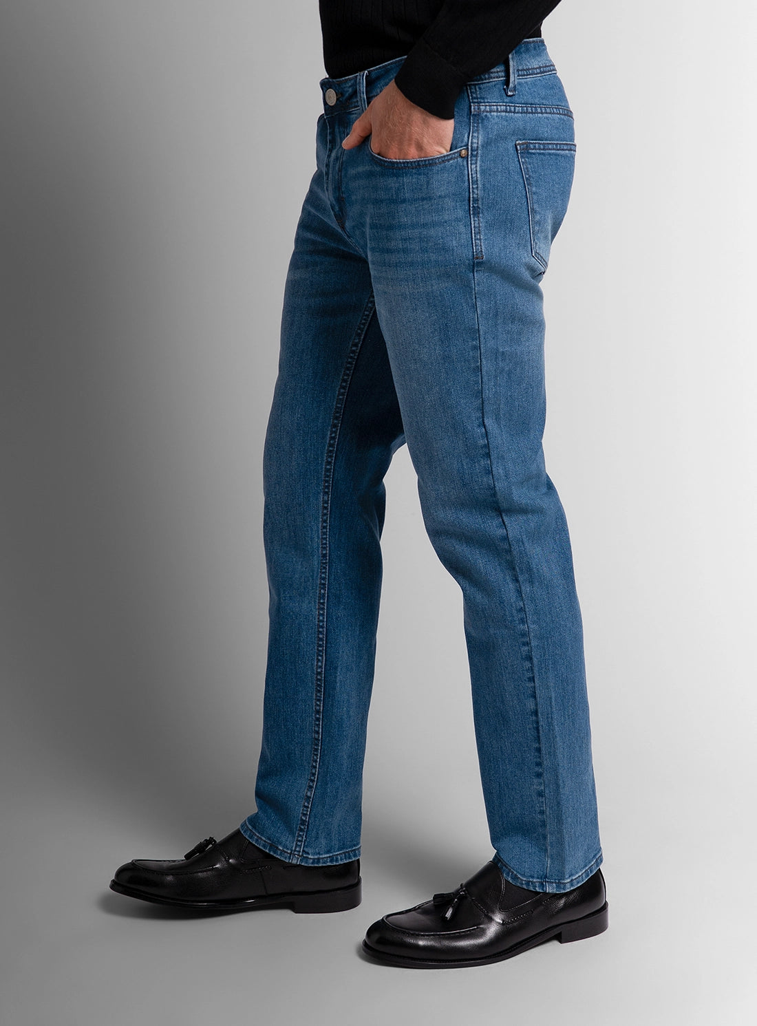 Person wearing blue jeans and black shoes on a gray background