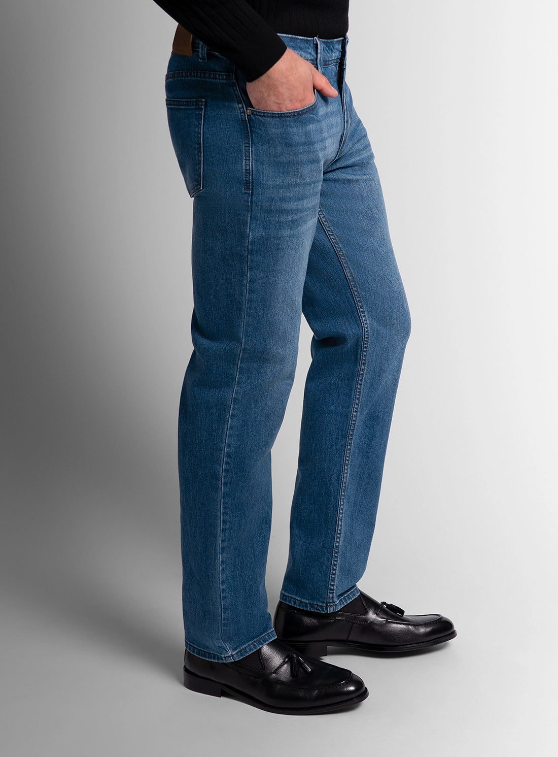 Person wearing blue jeans and black shoes on a gray background
