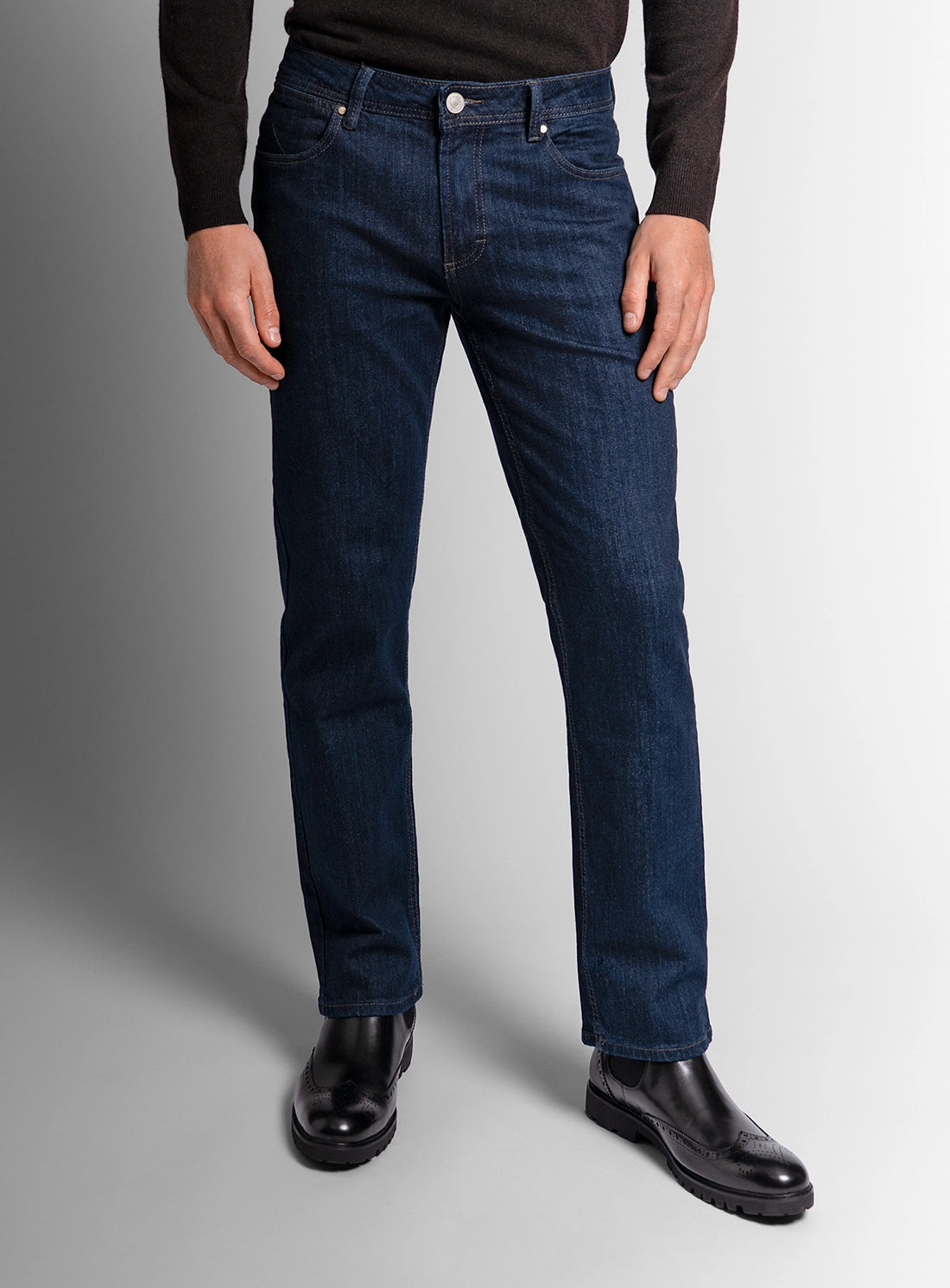 Person wearing dark blue jeans and black shoes on a gray background