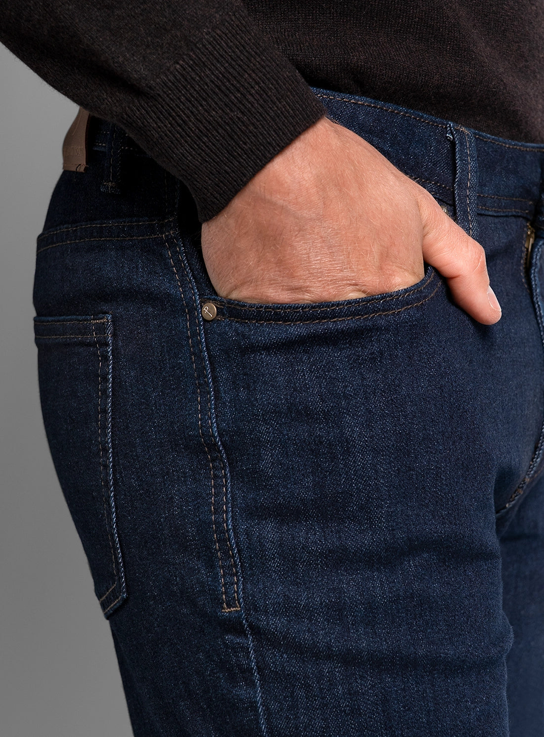 Close-up of a person wearing dark blue jeans with a gray background