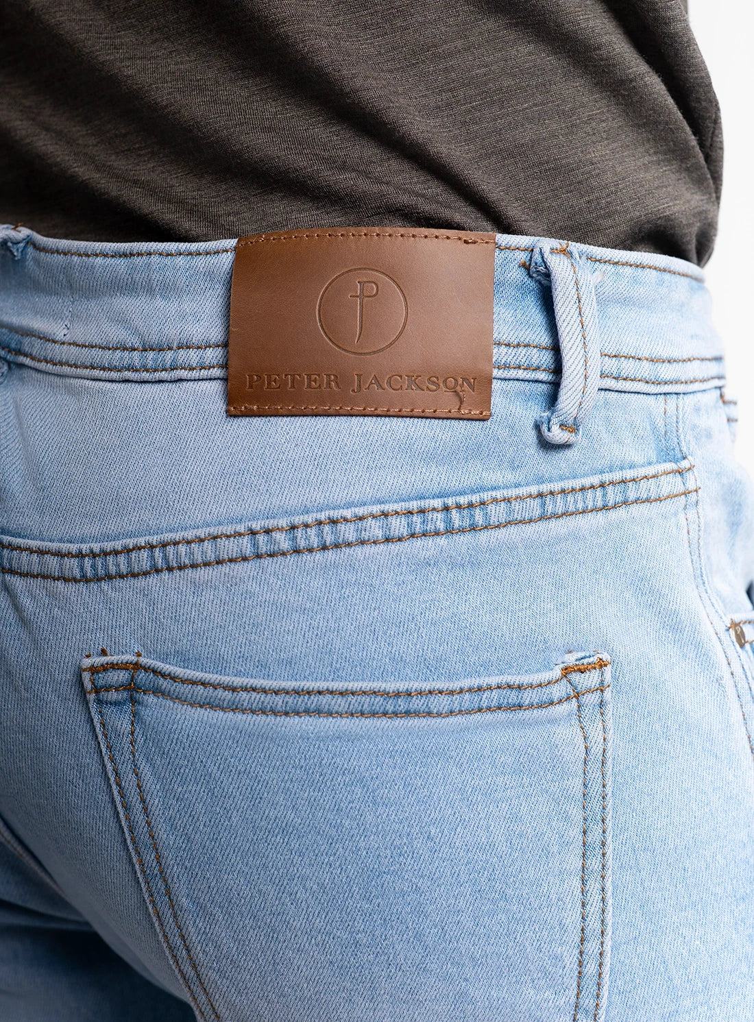 Light blue jeans with a brown leather patch displaying 'Peter Jackson' brand on a white background.