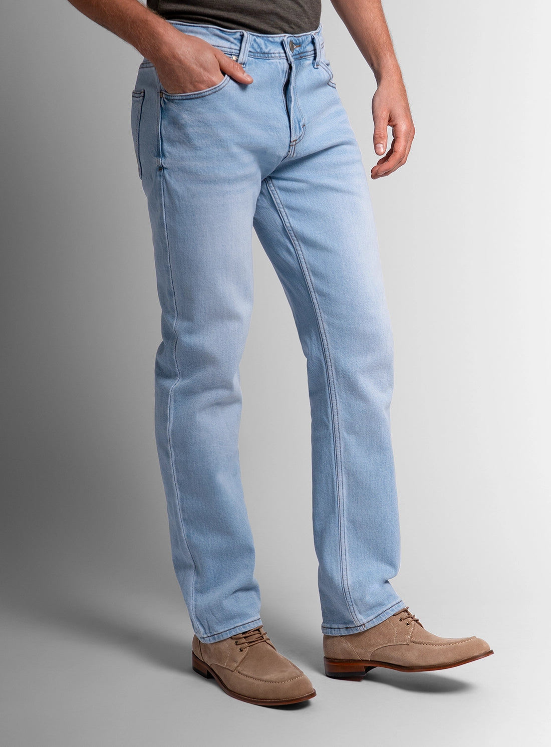 Person wearing light blue jeans and brown shoes on a gray background