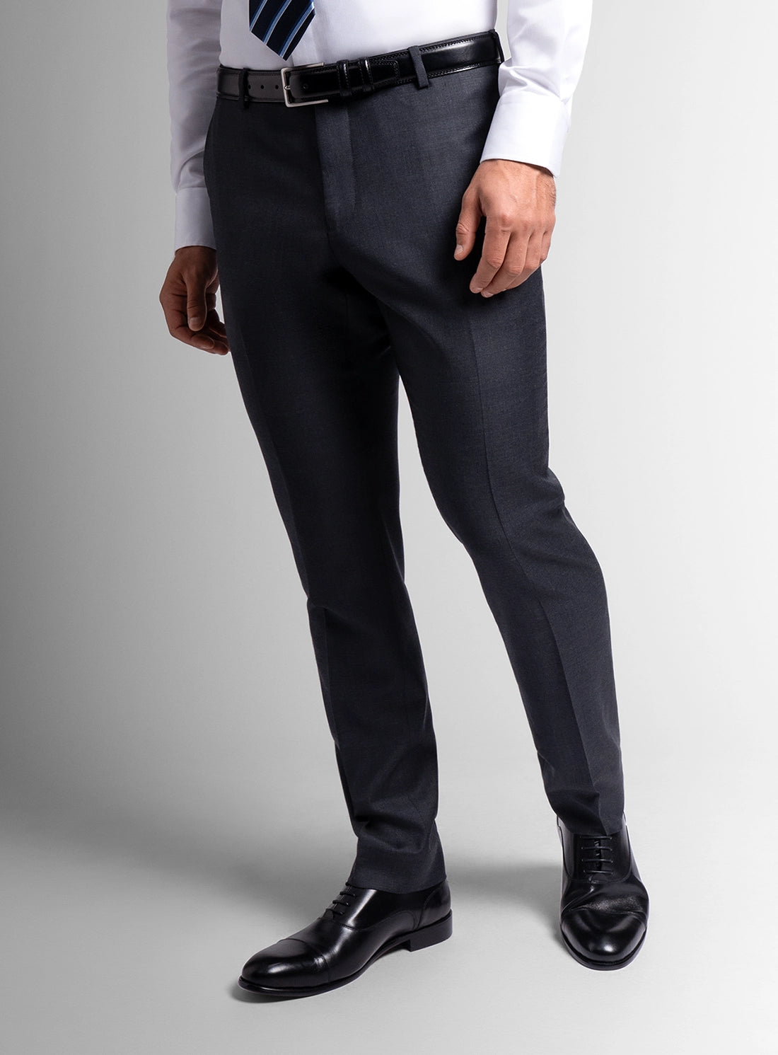 Dark gray dress pants worn with a white shirt and black shoes on a light gray background