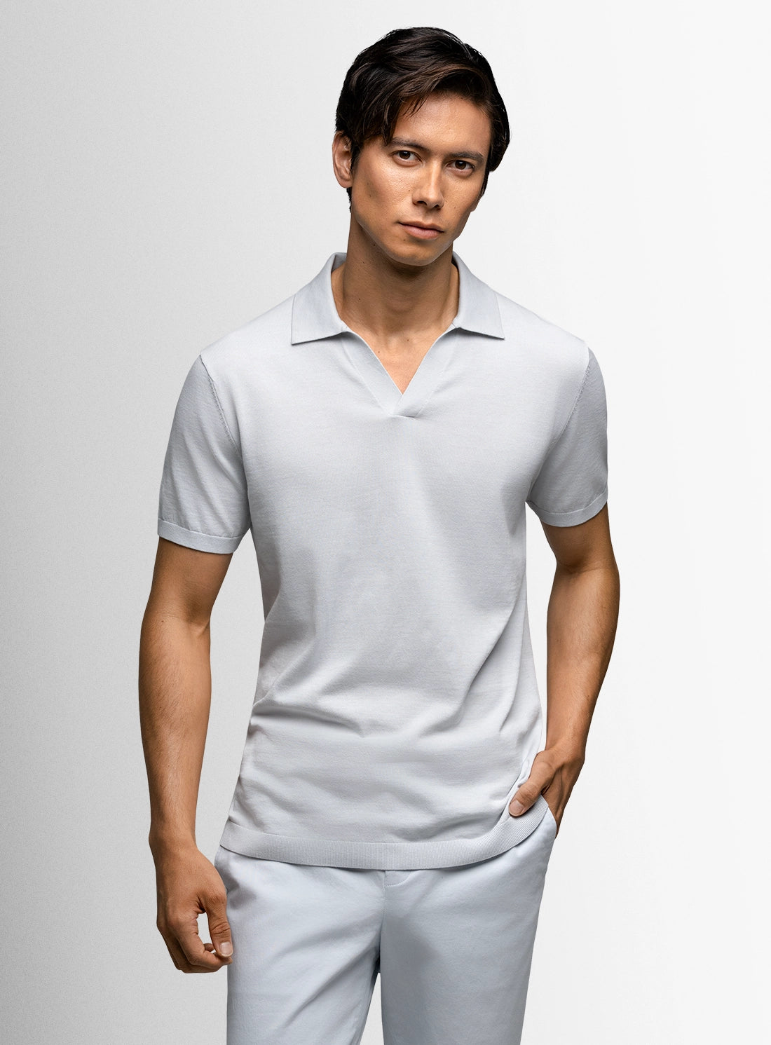 Man wearing a light gray polo shirt and white pants against a plain background