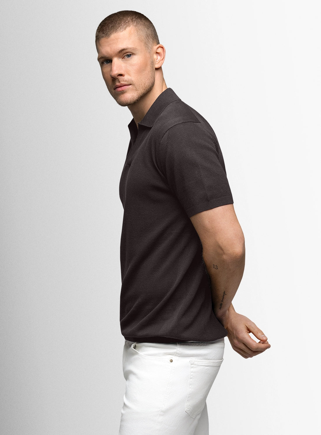Man wearing a black polo shirt and white pants on a light gray background