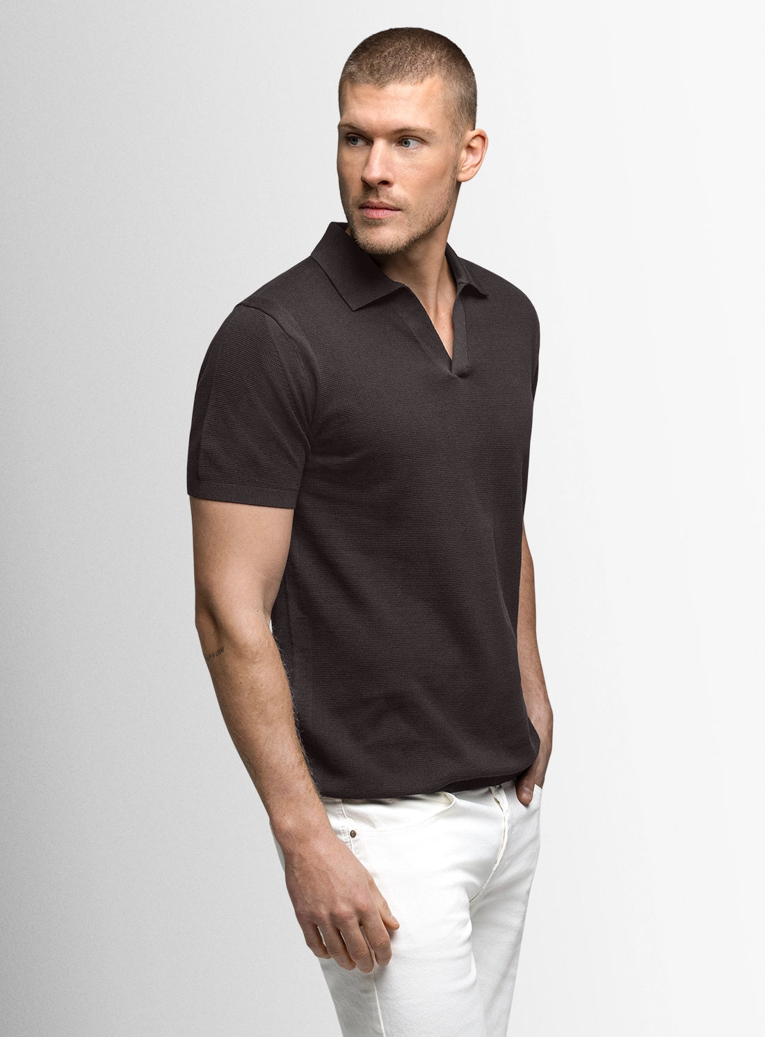 Man wearing a black polo shirt and white pants on a gray background