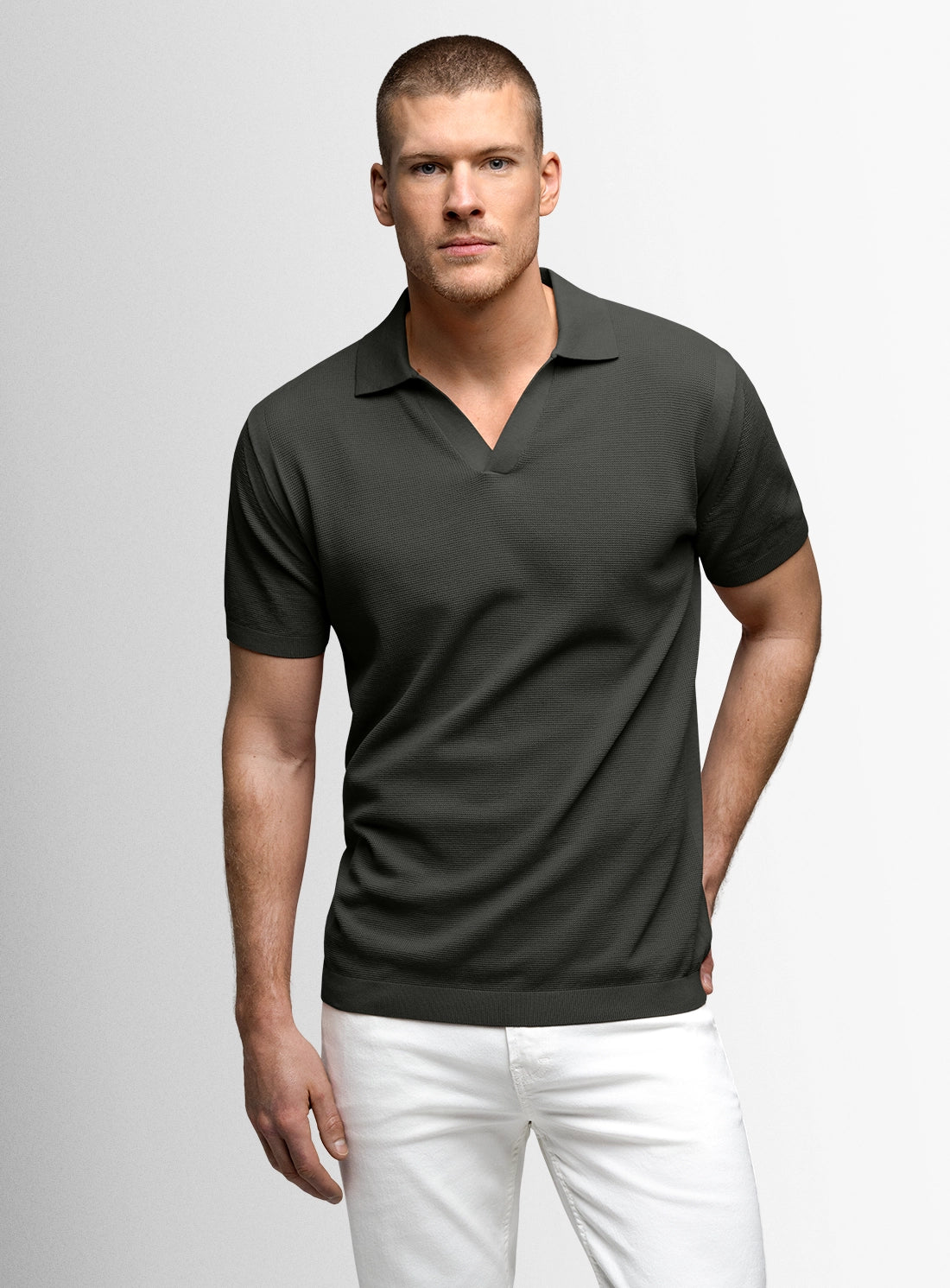 Man wearing a dark gray polo shirt and white pants on a light gray background