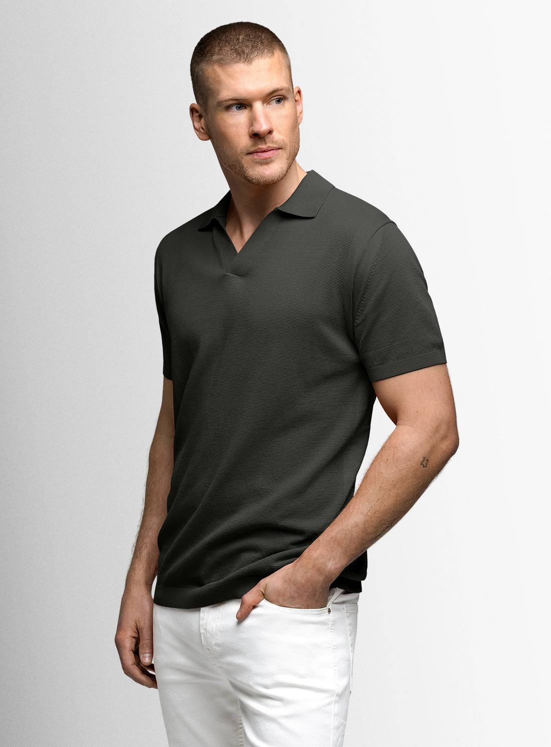 Man wearing a dark green polo shirt and white pants on a light gray background