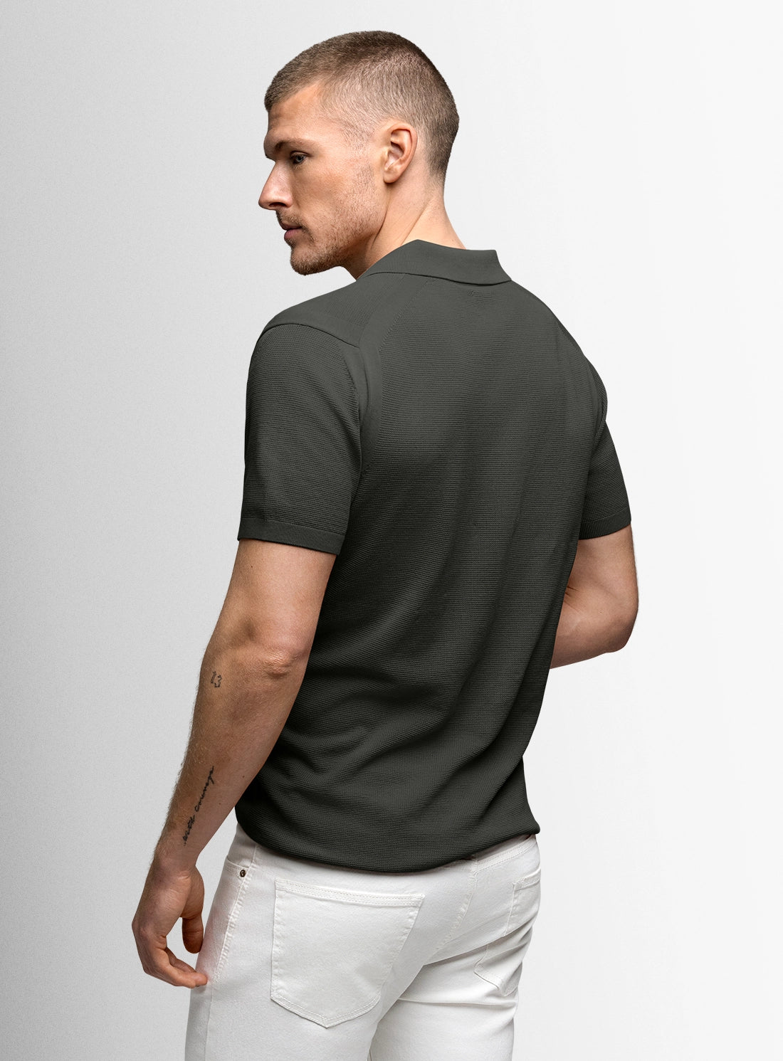 Man wearing a dark green polo shirt and white pants on a light gray background
