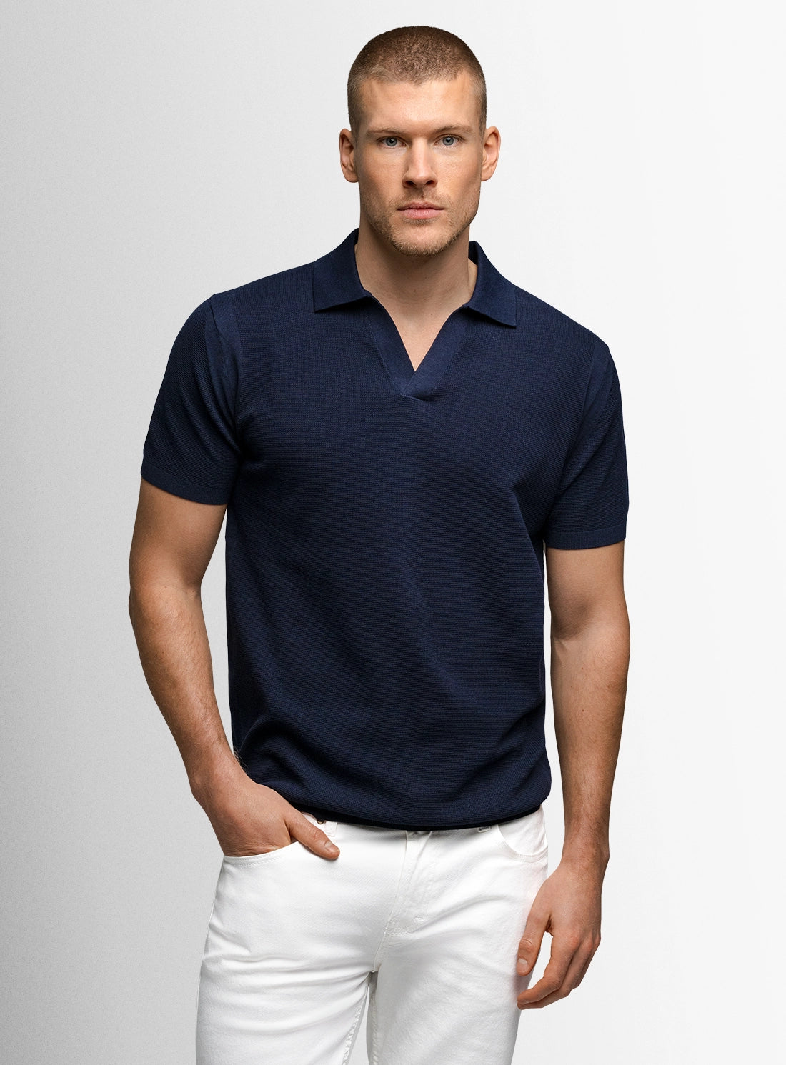 Man wearing a navy blue polo shirt and white pants on a light gray background