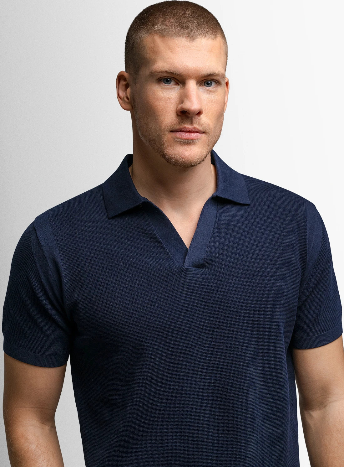 Man wearing a navy blue polo shirt against a light gray background