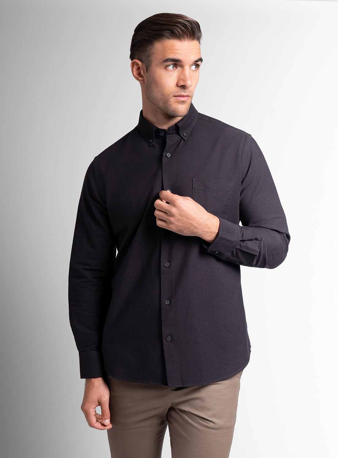 Man wearing a black button-up shirt and brown pants on a gray background