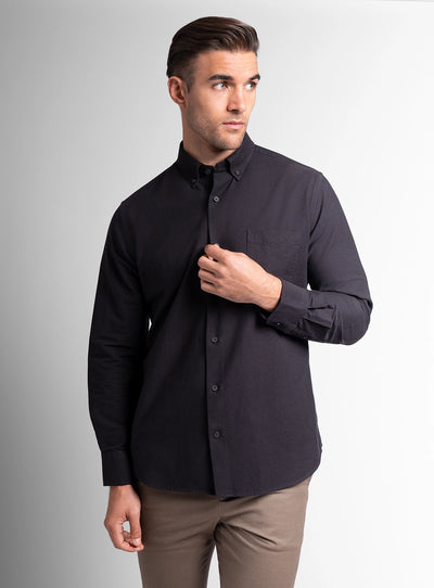 Man wearing a black button-up shirt and brown pants on a gray background