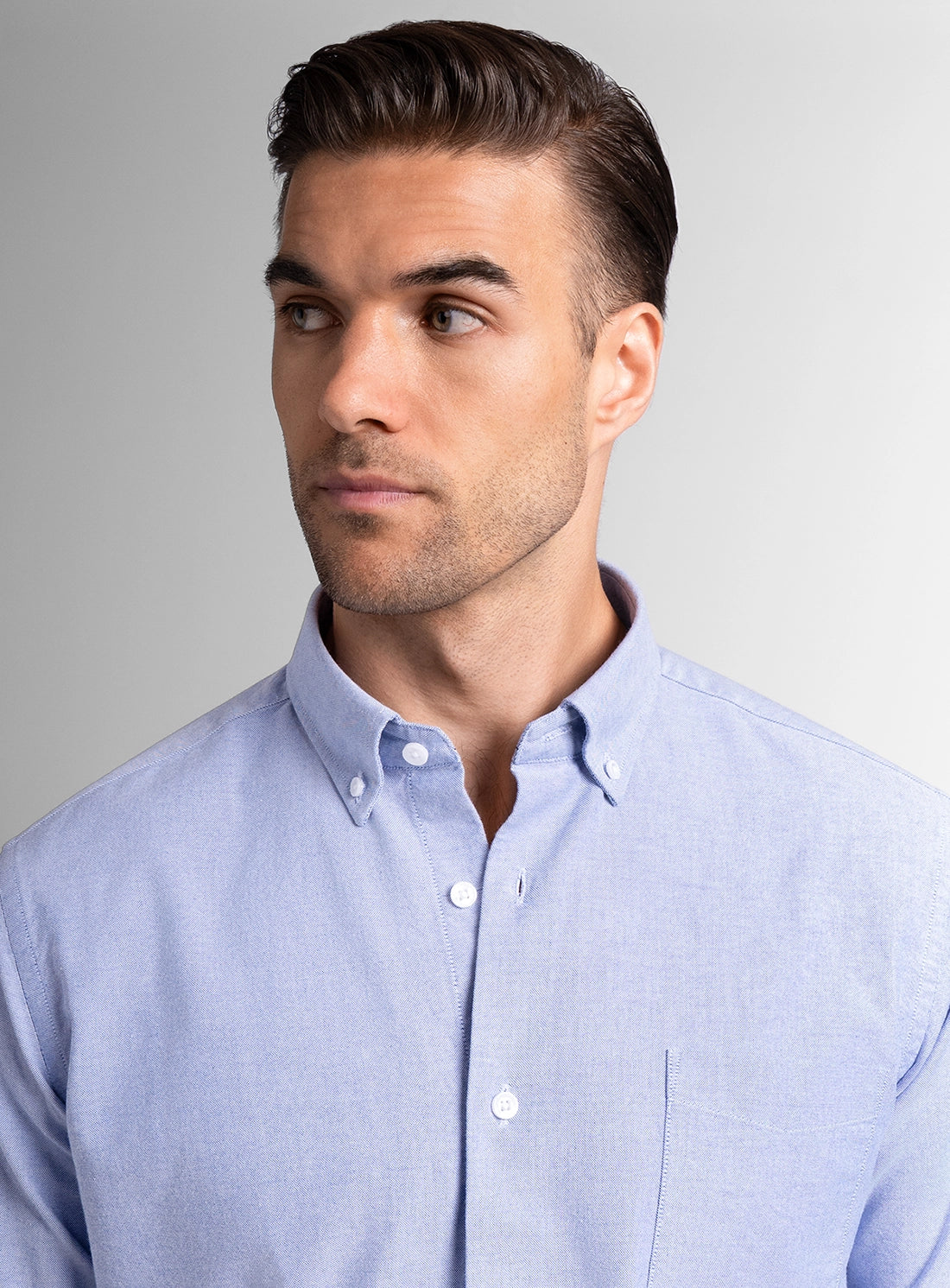Man wearing a light blue button-up shirt against a gray background