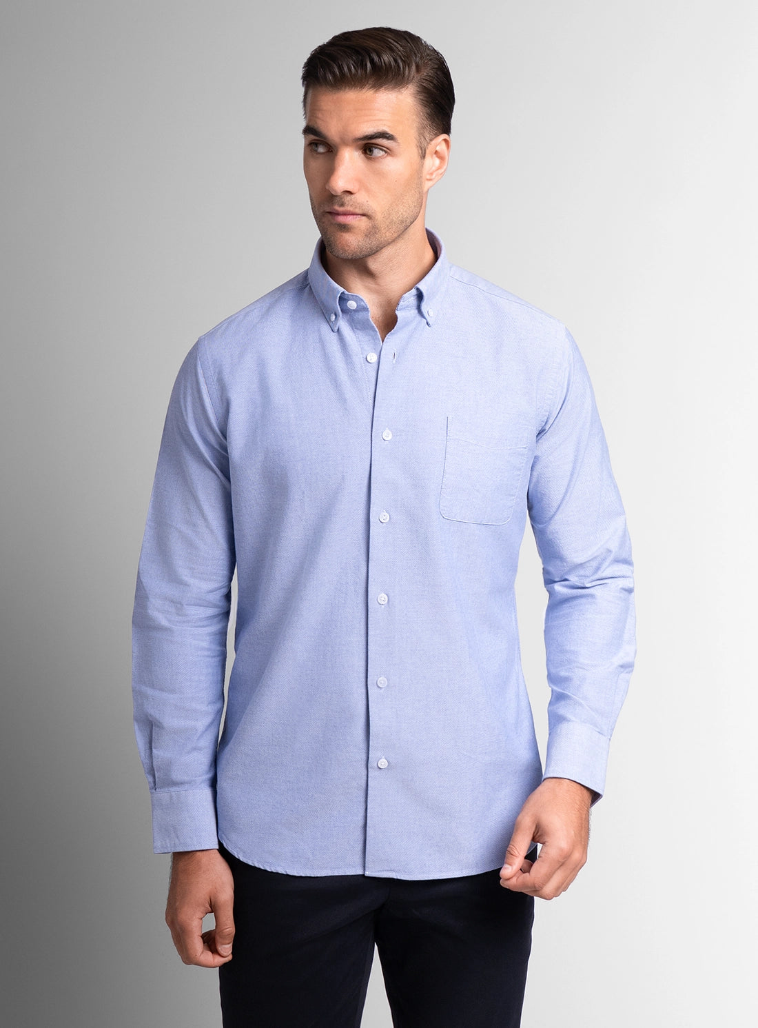 Man wearing a light blue button-up shirt against a gray background