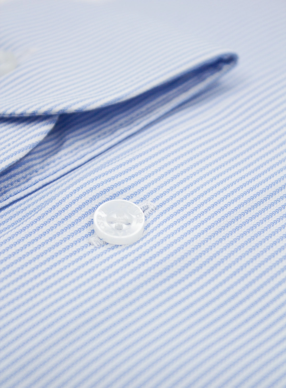 Close-up of a button on a light blue striped shirt