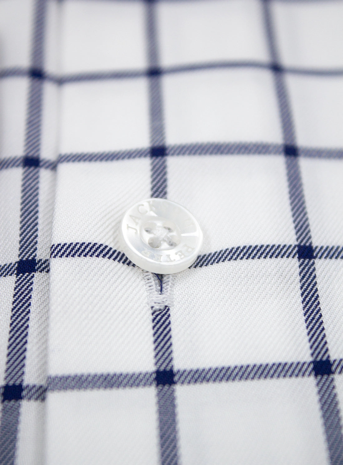 Close-up of a button on a checkered shirt with blue and white lines.