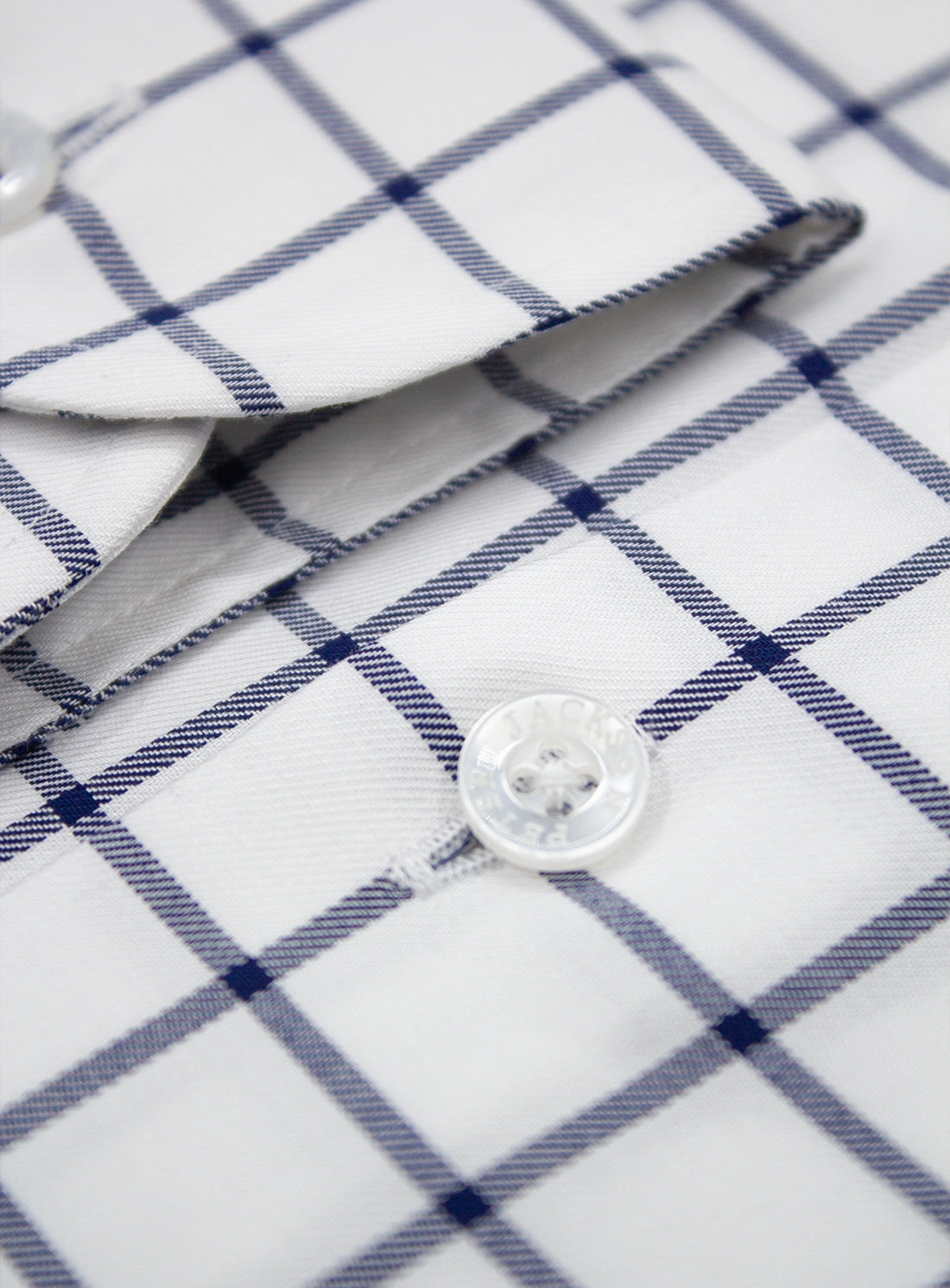 Close-up of a white shirt with blue checkered pattern and button details.