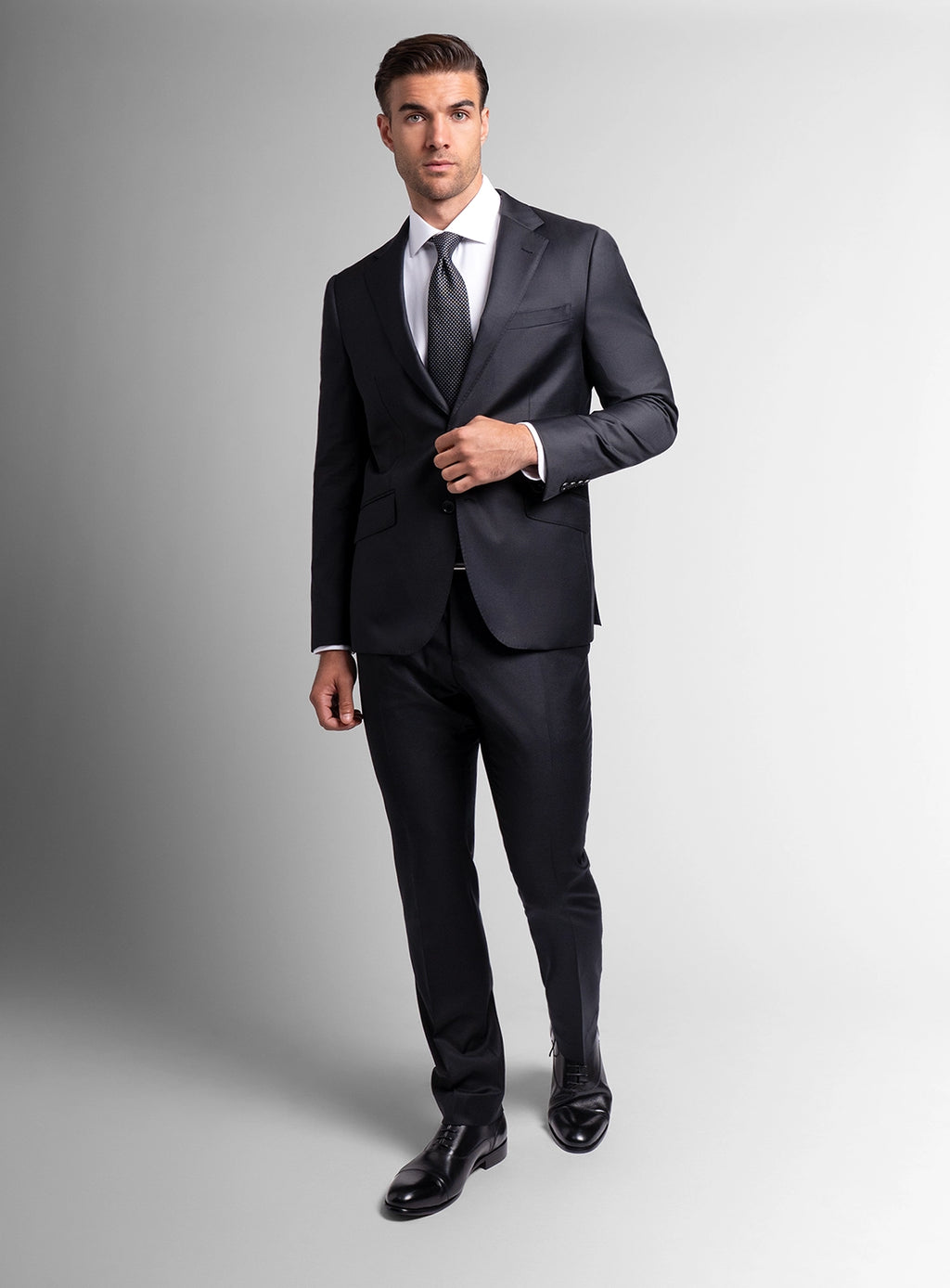 Man wearing a black suit with a white shirt and tie on a gray background