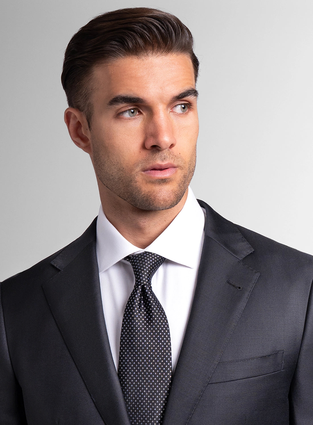 Man wearing a dark suit with a white shirt and patterned tie on a gray background