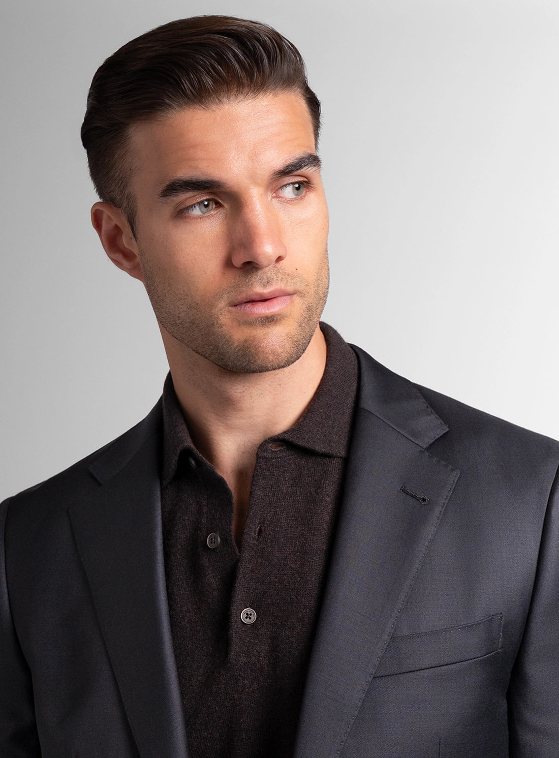 Man wearing a dark suit and brown shirt against a gray background