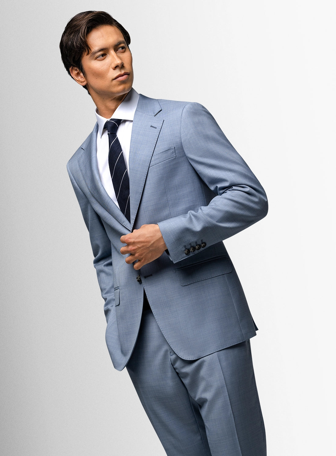 Man wearing a light blue suit with a white shirt and dark tie on a gray background