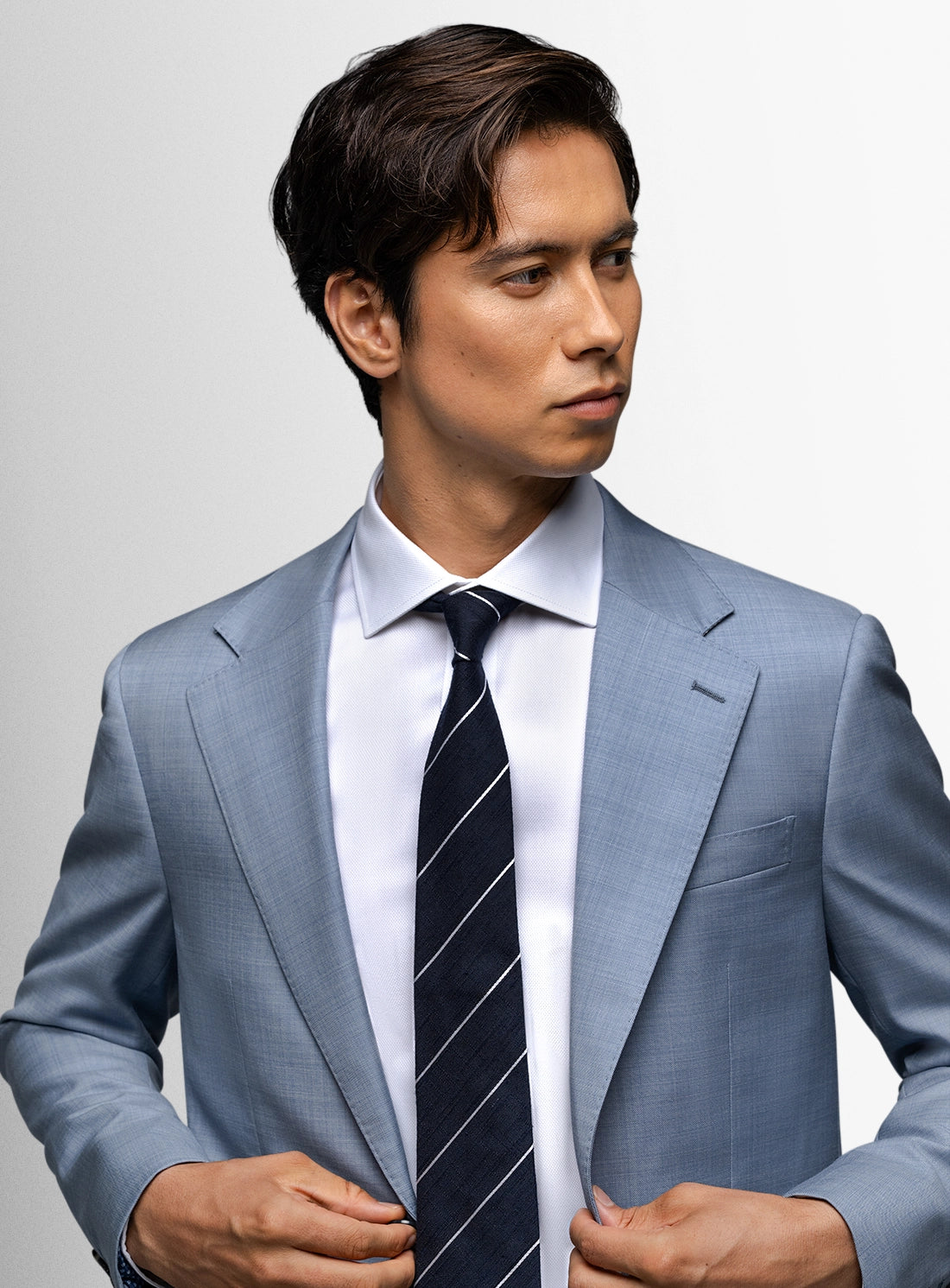 Man wearing a light gray suit with a striped tie on a plain background