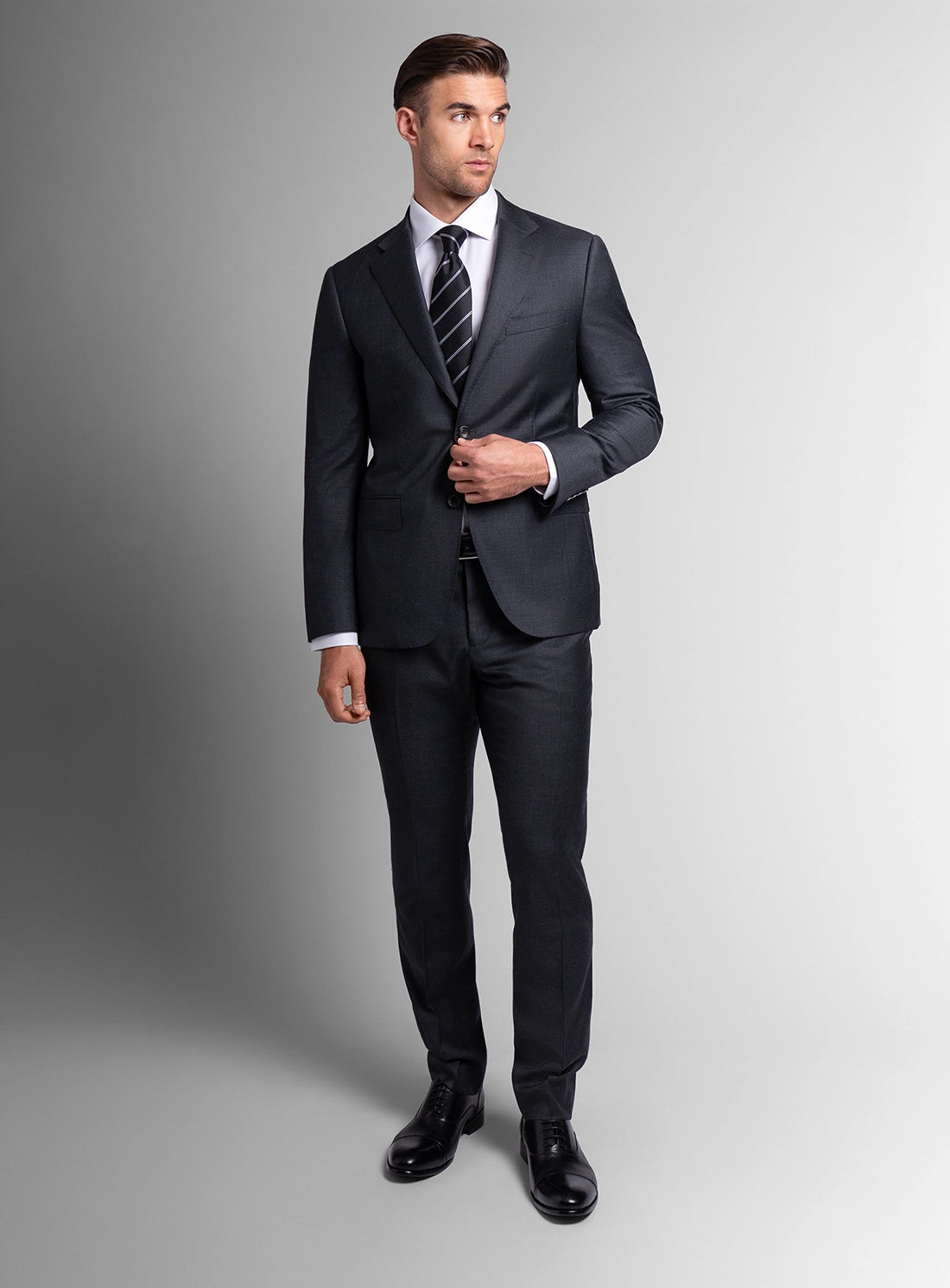 Man wearing a dark gray suit with a striped tie on a gray background