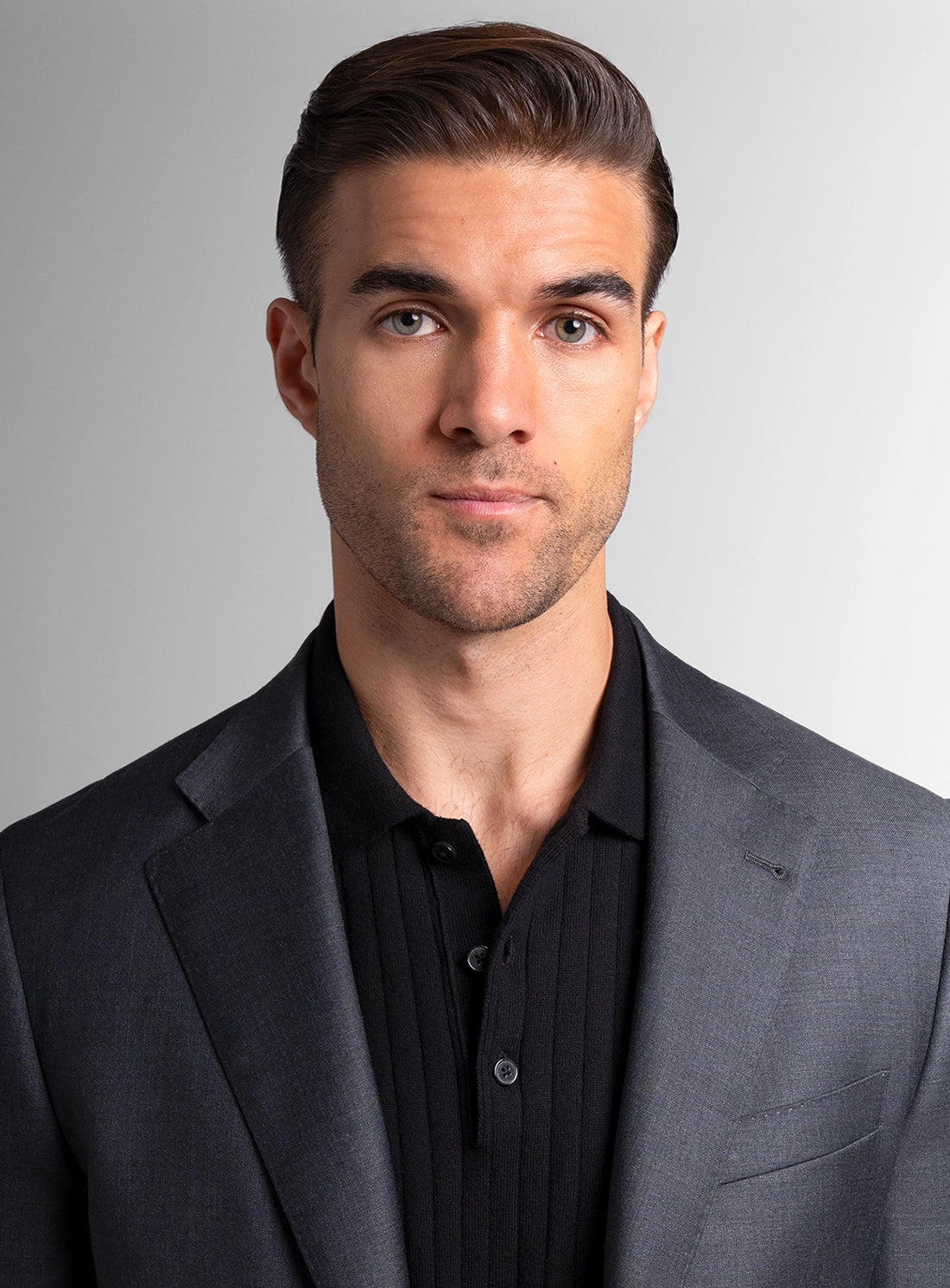 Man wearing a gray suit and black shirt against a gray background