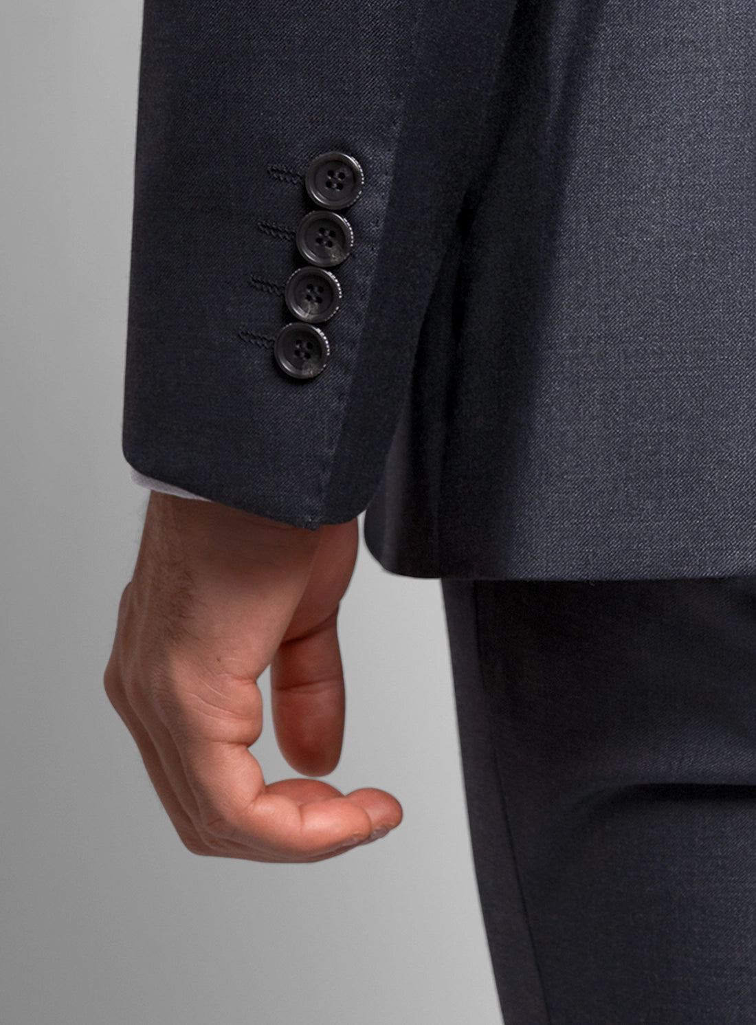 Close-up of a dark gray suit with three buttons on the sleeve against a neutral background