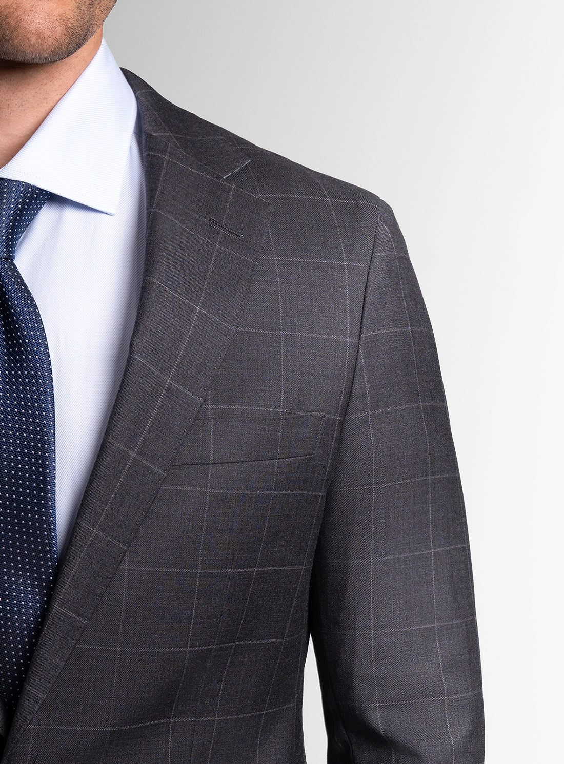 Gray checkered suit jacket with a white shirt and blue tie on a light gray background