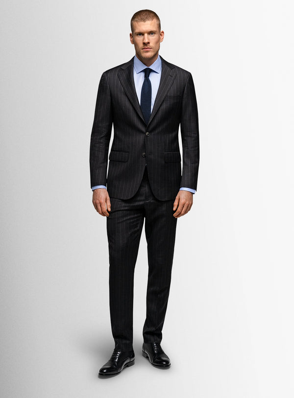 Man wearing a dark pinstripe suit with a white shirt and blue tie on a light gray background