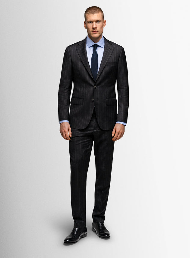 Man wearing a dark pinstripe suit with a white shirt and blue tie on a light gray background