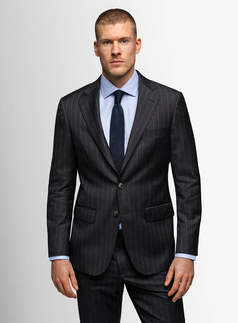 Man wearing a dark pinstripe suit with a light blue shirt and dark tie on a plain background
