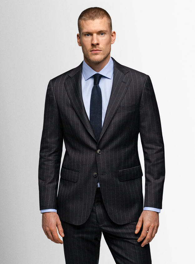 Man wearing a dark pinstripe suit with a light blue shirt and dark tie on a plain background
