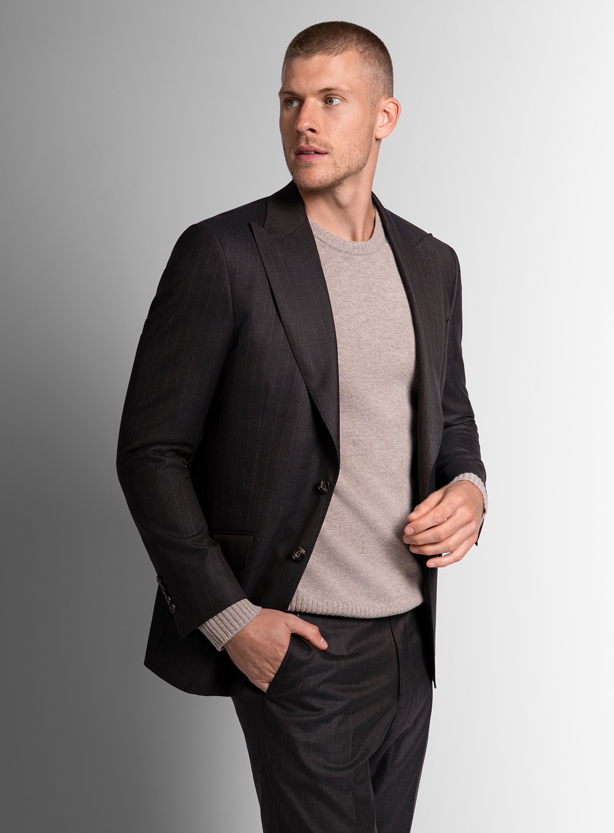 Man wearing a brown blazer over a gray sweater on a gray background