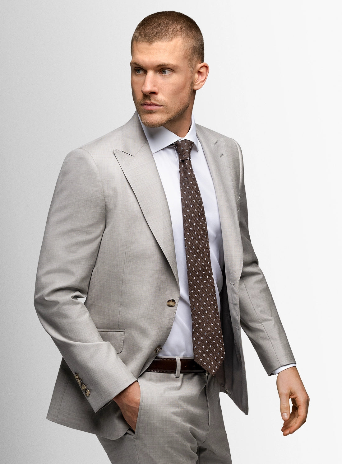 Man wearing a gray suit with a white shirt and patterned tie on a light gray background