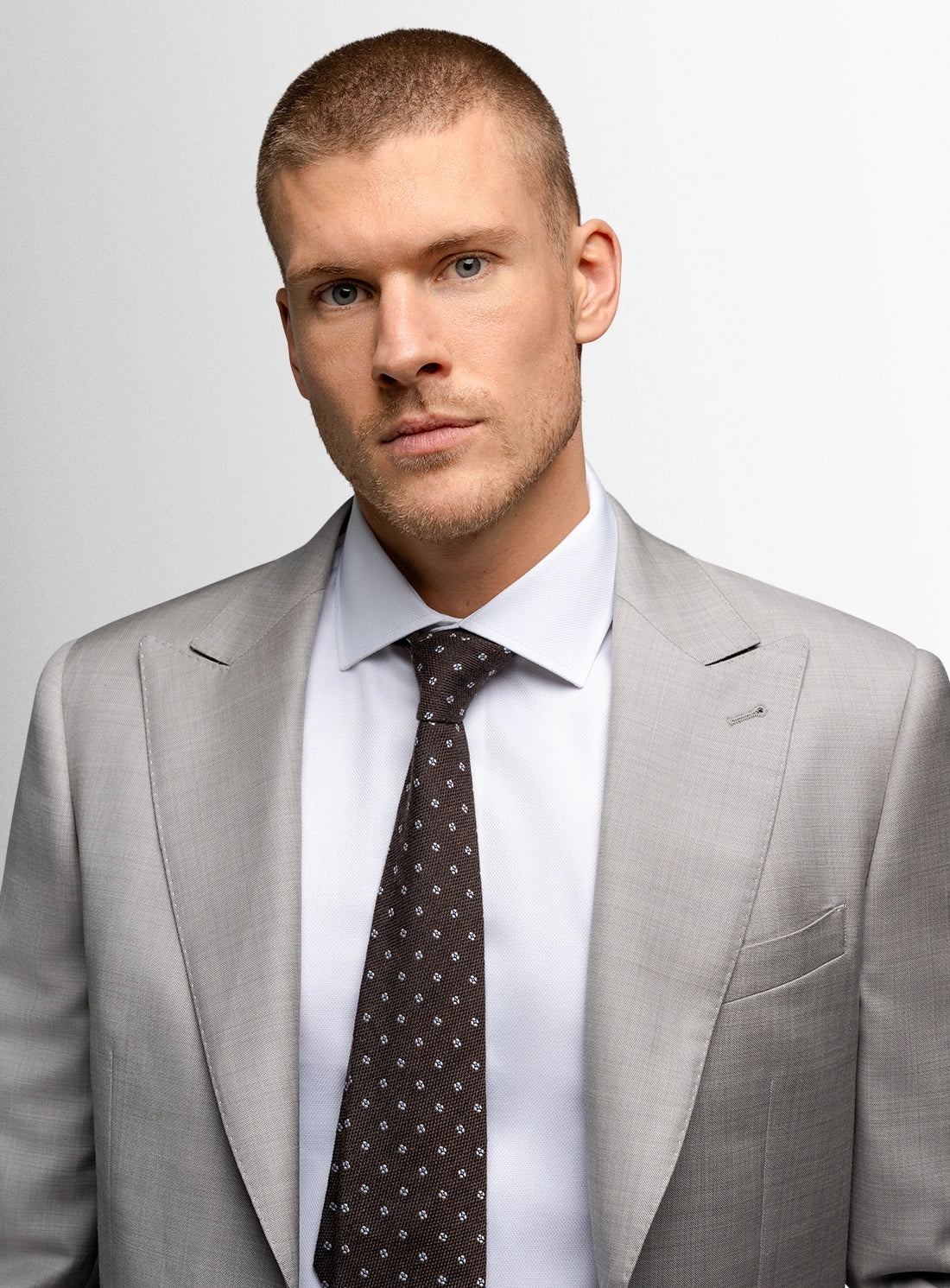 Man wearing a gray suit with a white shirt and patterned tie on a light gray background