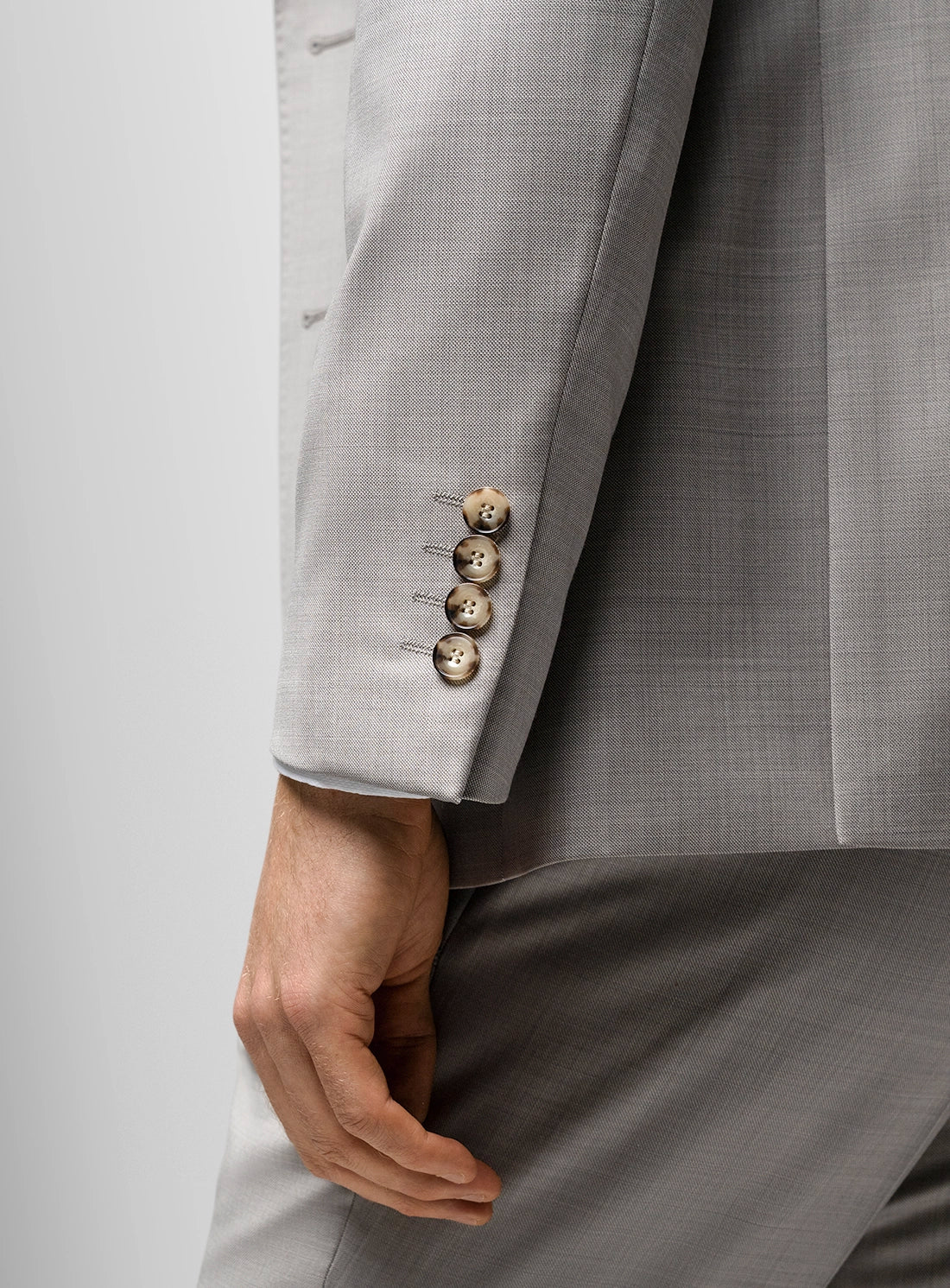 Gray suit jacket with buttons and a hand visible on a light gray background