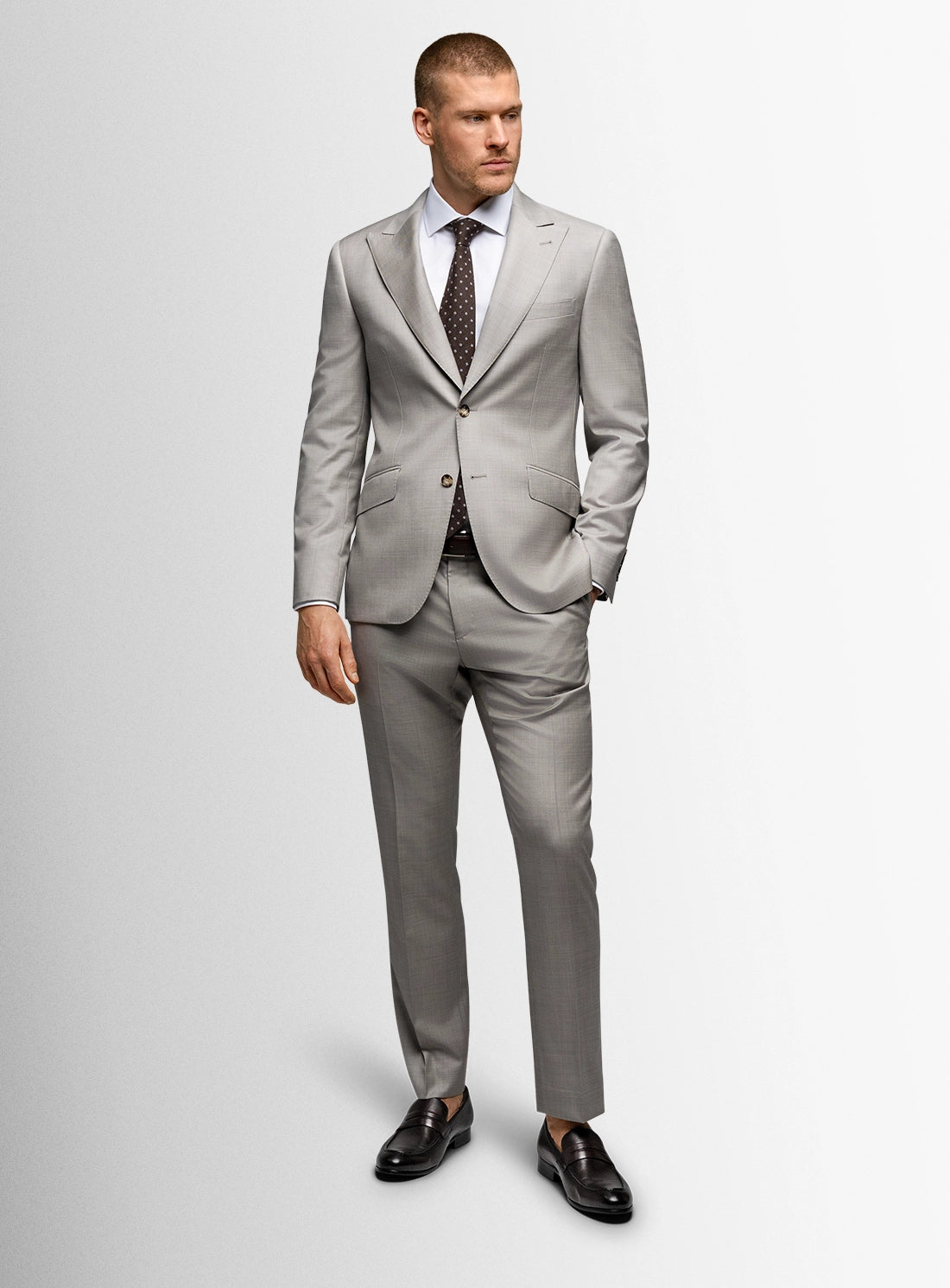 Man wearing a gray suit with a white shirt and patterned tie on a light gray background