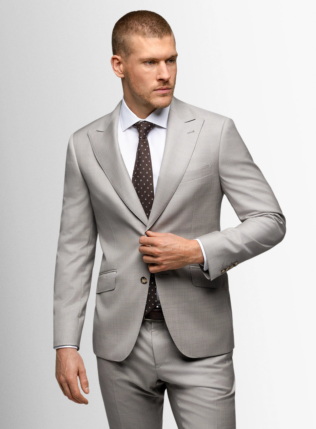 Man wearing a light gray suit with a patterned tie on a plain background