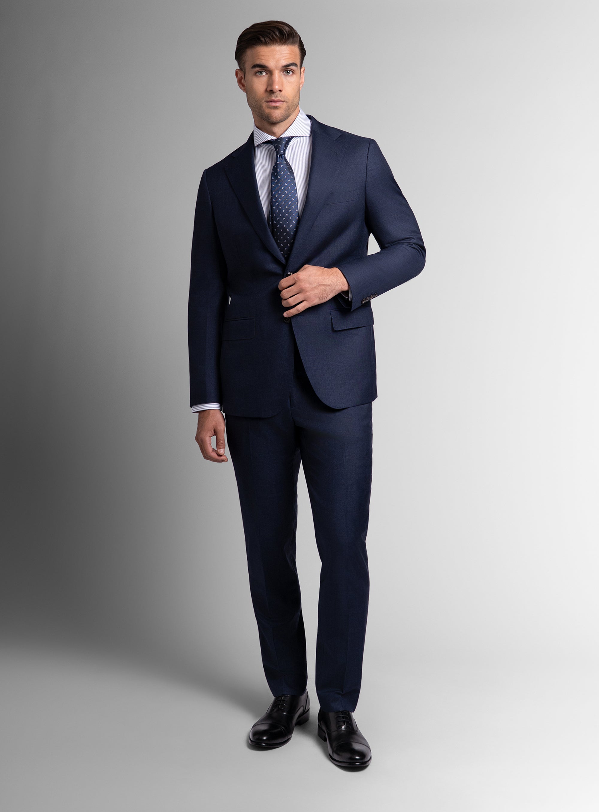 Man wearing a navy suit with a white shirt and patterned tie on a gray background