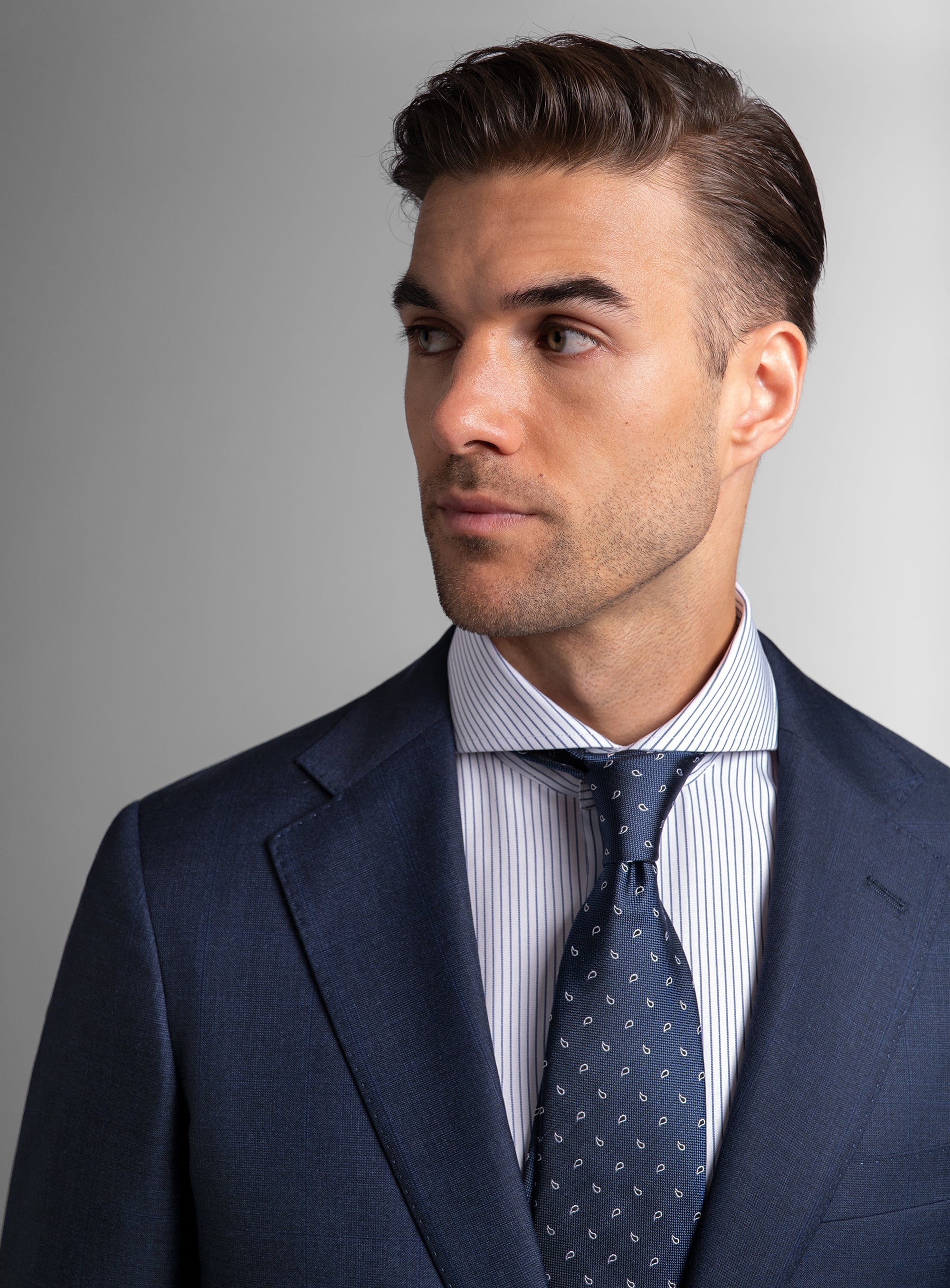 Man wearing a navy suit with a patterned tie against a gray background