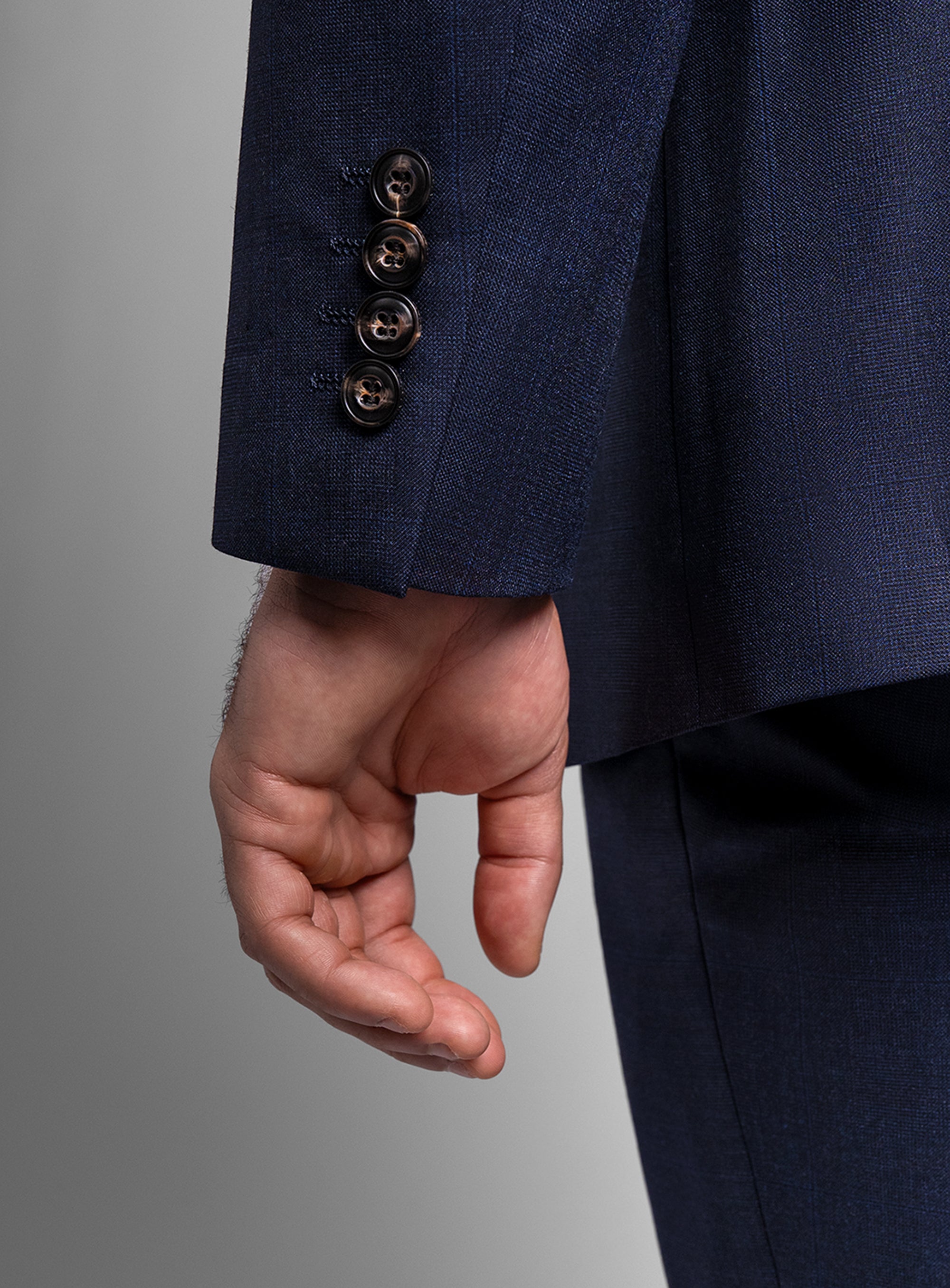 Close-up of a hand wearing a navy blue suit with three buttons on a gray background