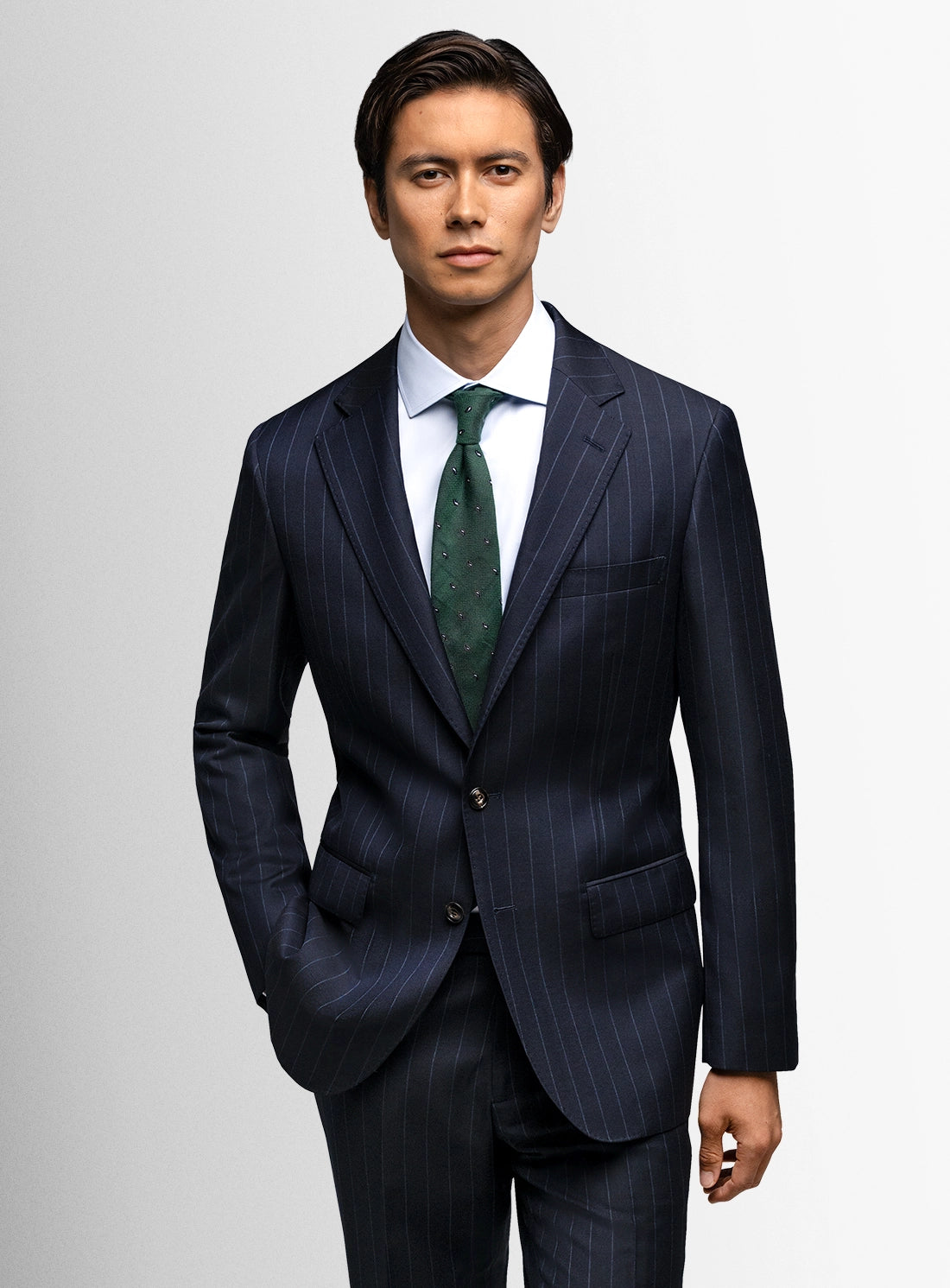 Man wearing a dark pinstripe suit with a green tie on a light gray background