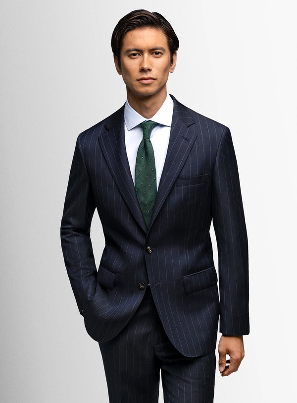 Man wearing a dark pinstripe suit with a green tie on a light gray background
