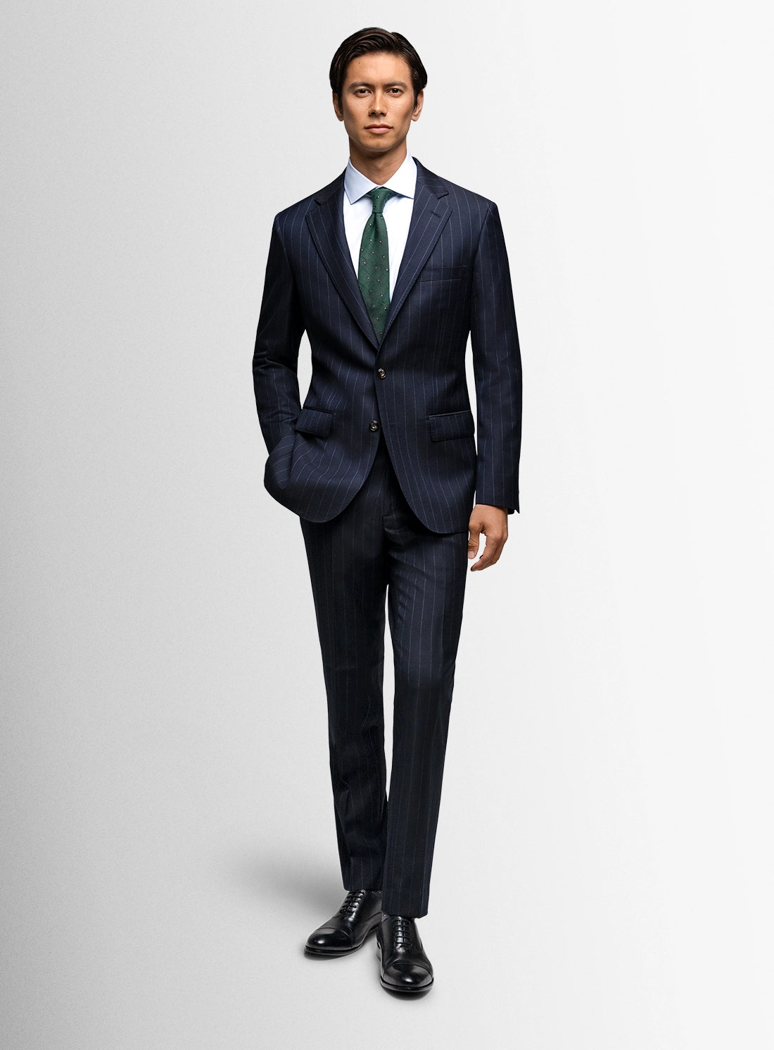 Man wearing a dark blue suit with a green tie on a light gray background